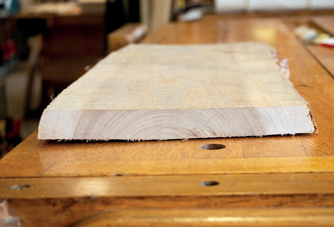 Rough-sawn hardwood board resting on a workbench, showing its growth rings and natural edge