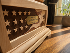 Close-up of the Heirloom Sentinel memorial urn featuring handcrafted American flag intarsia, carved eagle artwork, personalized veteran plaque, and solid hardwood construction illuminated by natural window light.